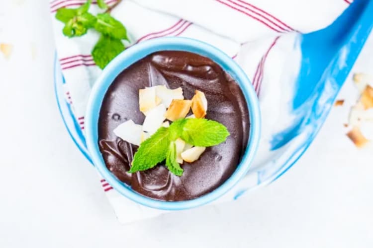 A blue bowl with vegan chocolate pudding topped with coconut and mint