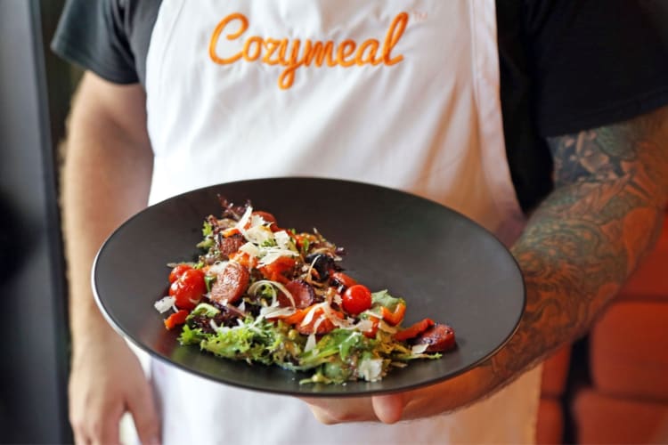 A person in a Cozymeal apron holding a salad