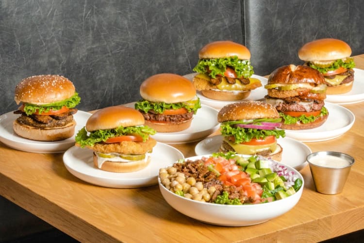 Different types of burgers and a salad on a wooden table