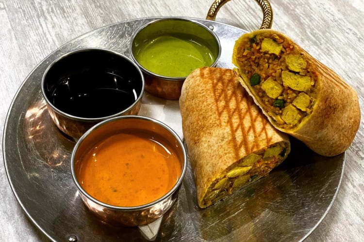 A wrap on a silver plate next to three dipping sauces