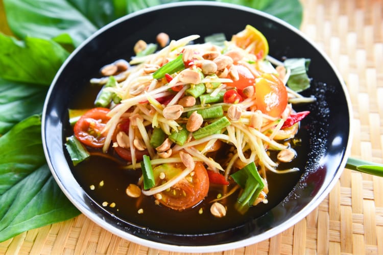A bowl of papaya salad surrounded by Thai basil leaves