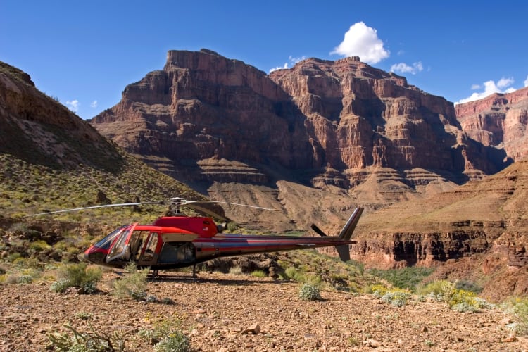 A red helicopter on the ground surrounded by red rock mountains