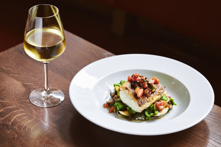 A fish dish next to a glass of white wine