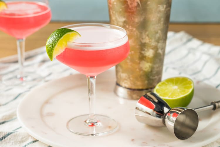 A pink beverage in a coupe glass with lime