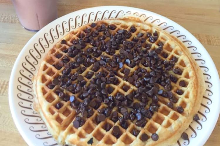 A waffle with chocolate chips and a cup of chocolate milk