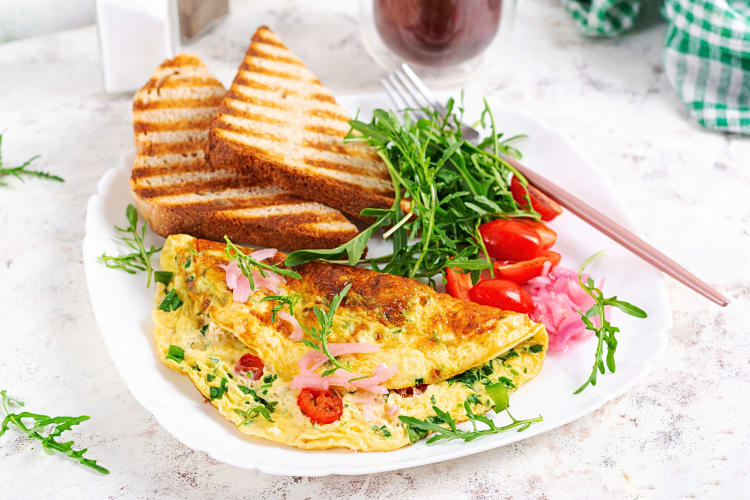 An omelette and toast on a plate, paired with tomatoes and greens