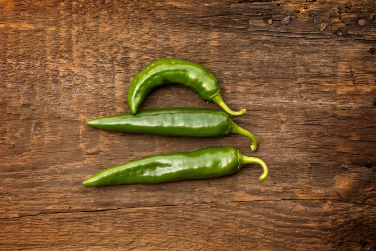 Three Anaheim peppers on a wooden board.