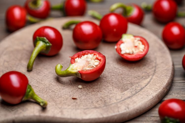 Cherry peppers on a wooden board, some sliced in half to reveal their seeds.