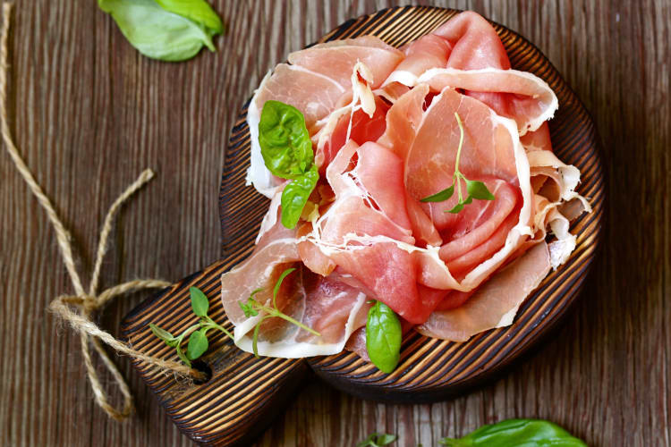 Top view of pieces of prosciutto with green leaves on a wooden chopping board
