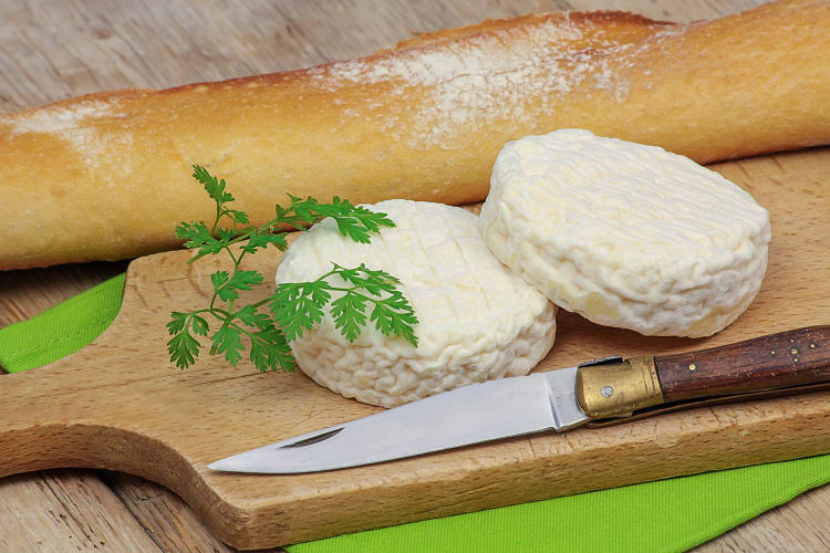 Two wheels of goat cheese in between a knife and bread
