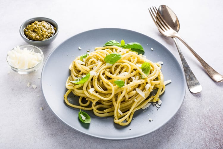 Linguine pasta topped with basil, next to bowls of pesto and cheese