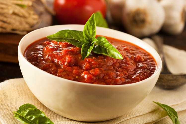 Marinara sauce in a white bowl topped with a sprig of leaves