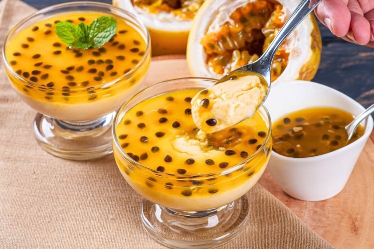 Two passion fruit desserts next to a bowl with pulp and seeds