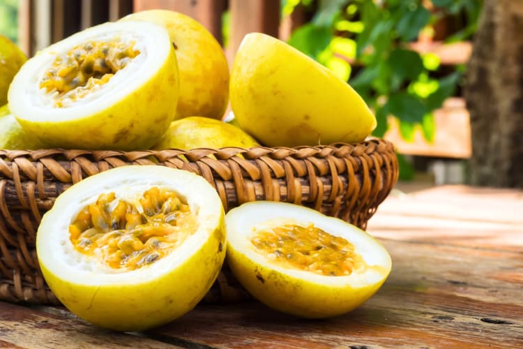 Whole and halved passion fruit on a table and in a bowl