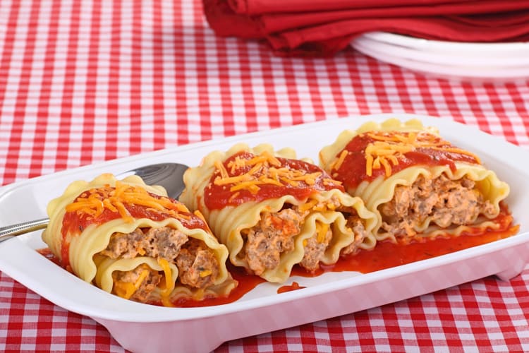 Three portions of lasagna in a white bowl topped with cheese and sauce