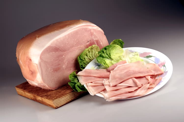 Full portion of prosciutto cotto with slices next to it on a plate