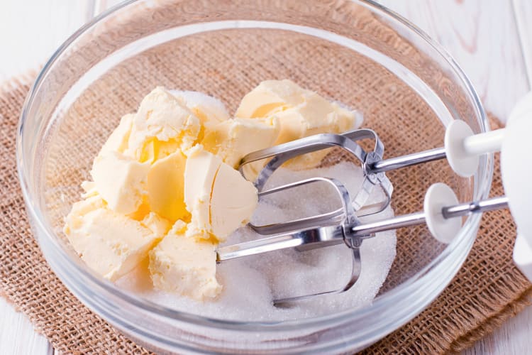 Butter in a bowl with sugar and the blending hands of an electric blender