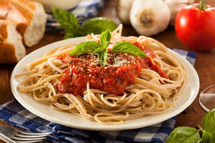 Spaghetti on a plate topped with marinara and basil leaves