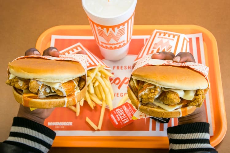 A person holding two chicken sandwiches over an orange tray