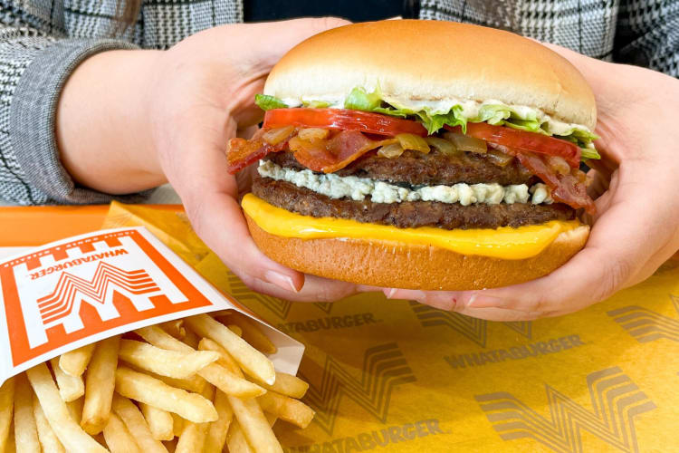 A person holding a burger next to some fries