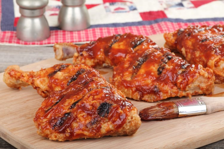 Three pieces of chicken on a wooden chopping board with a basting brush