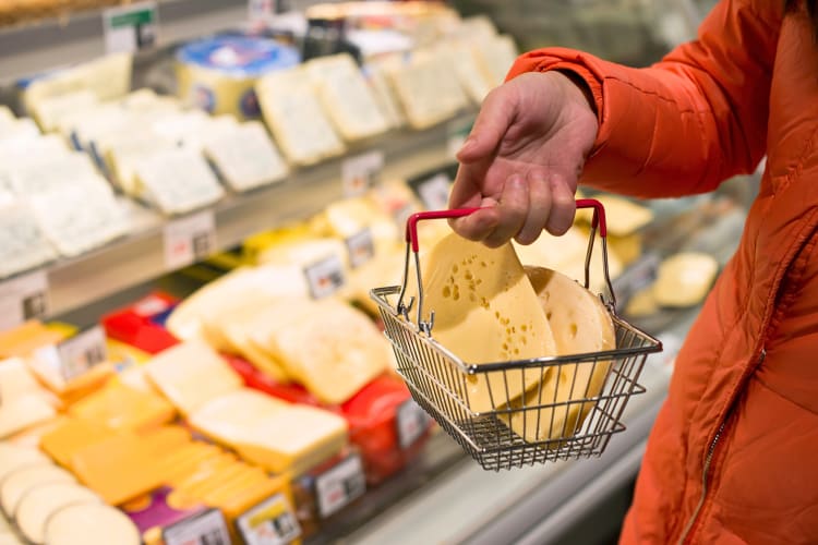 Person's hand holding a small basket with two blocks of cheese in, buying at the supermarket