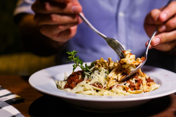 Close-up of hands scooping up Tagliatelle pasta with a fork and spoon