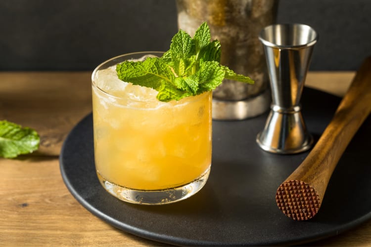 A yellow drink with mint next to a muddler and cocktail measurer