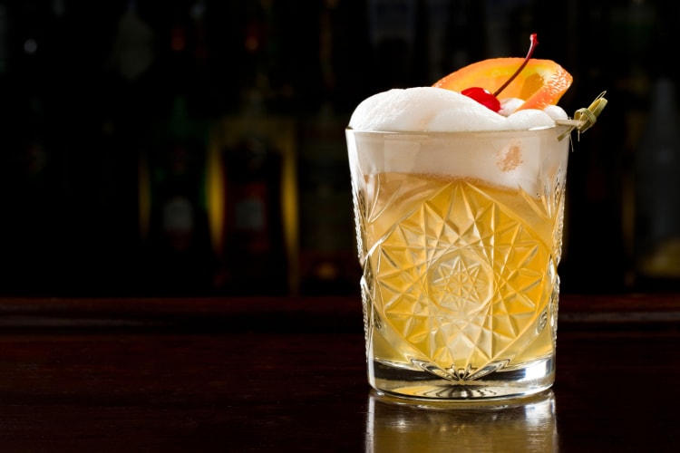 A cocktail with egg white foam, a cherry and an orange slice