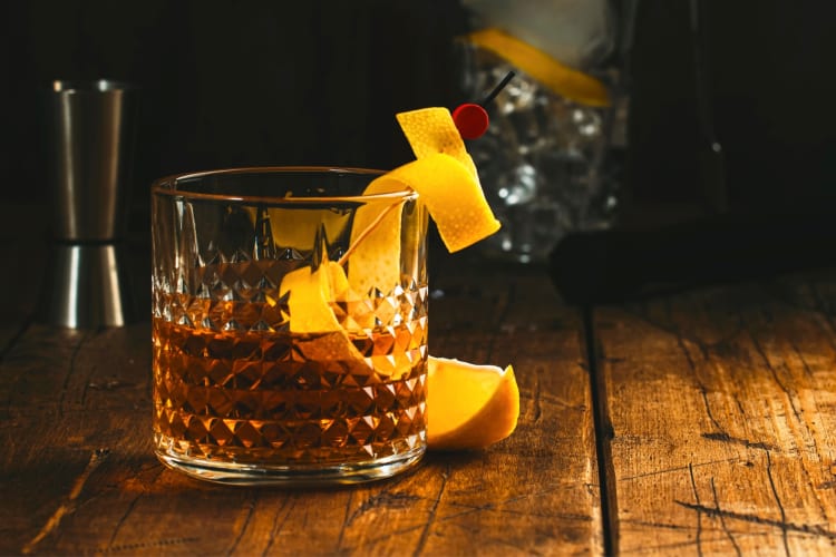 A whiskey cocktail with orange peel on a wooden surface