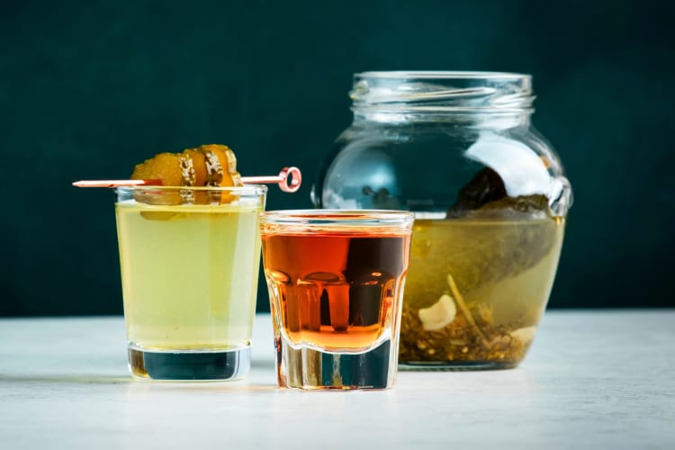 A shot of whiskey and a shot of pickle juice next to a pickle jar