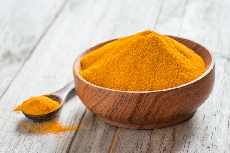 Orange tumeric powder in a wooden bowl with a wooden spoon next to it 