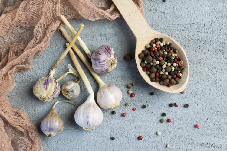 Garlic bulbs next to peppercorns in a wooden spoon