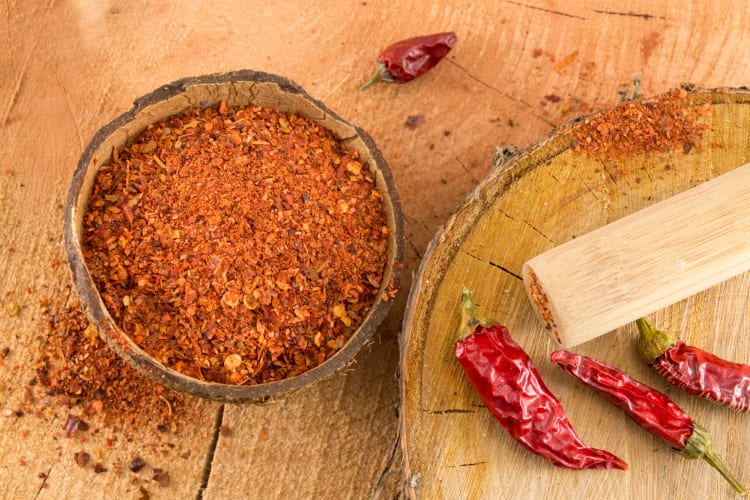 Whole cayenne peppers and crushed cayenne pepper on a wooden surface