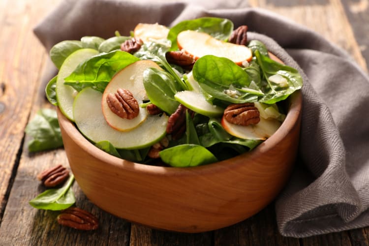 A spinach salad with apple slices and pecans