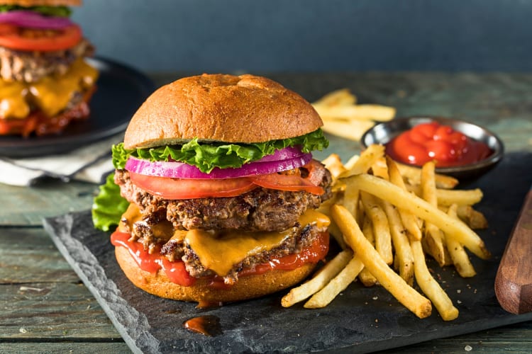Double cheeseburger with lettuce, tomato and onions, next to a portion of fries