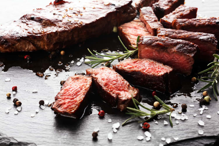 Close-up shot of a cut up rib eye steak with garnish, salt and pepper grindings on top