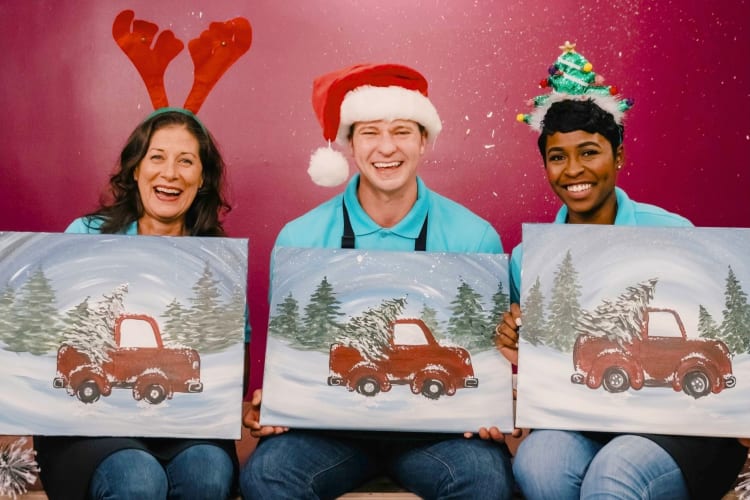 Three people holding holiday paintings