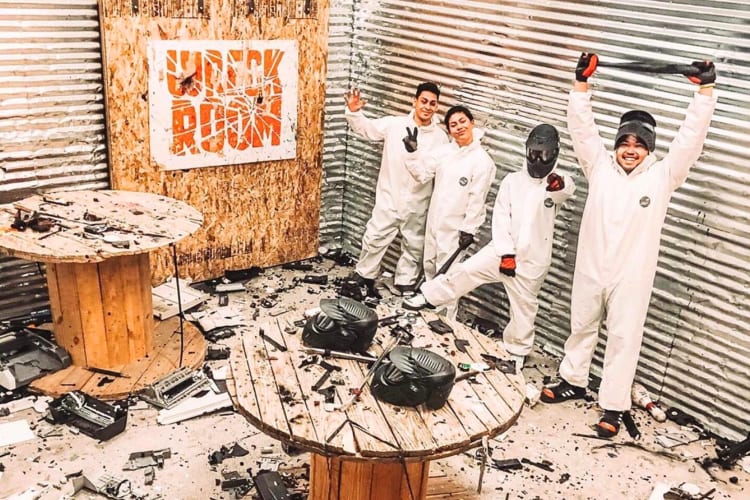 Four people posing for a photo at Wreck Room, surrounded by destroyed goods
