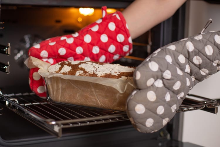 A person taking bread out of the oven with oven mitts