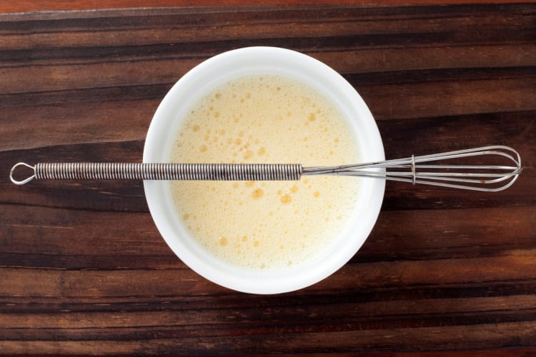 A bowl with whisked eggs and a whisk on top