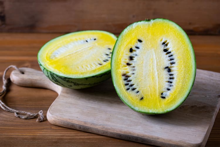 A yellow watermelon cut in half on a wooden chopping board