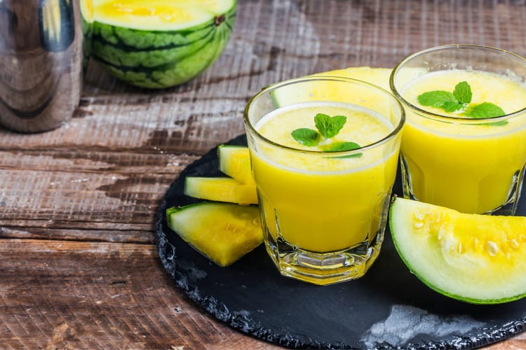 Two glasses with yellow drinks next to pieces of yellow watermelon