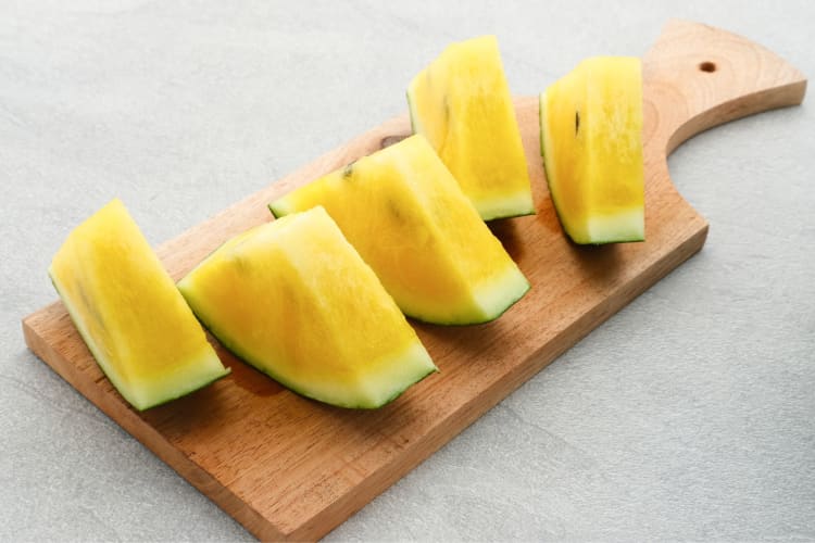 Triangle slices of yellow watermelon on a wooden chopping board