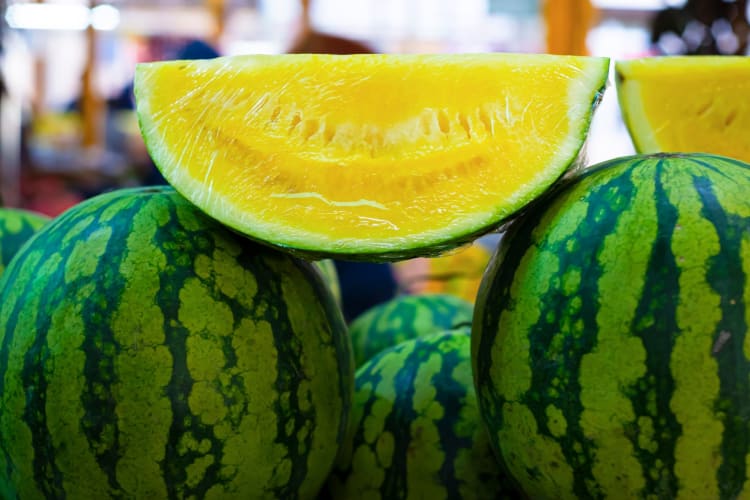 Whole green rind watermelons with a slice of yellow watermelon on top