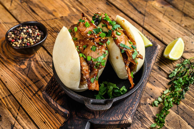 Two pork bao buns served in a pan on top of a wooden serving board