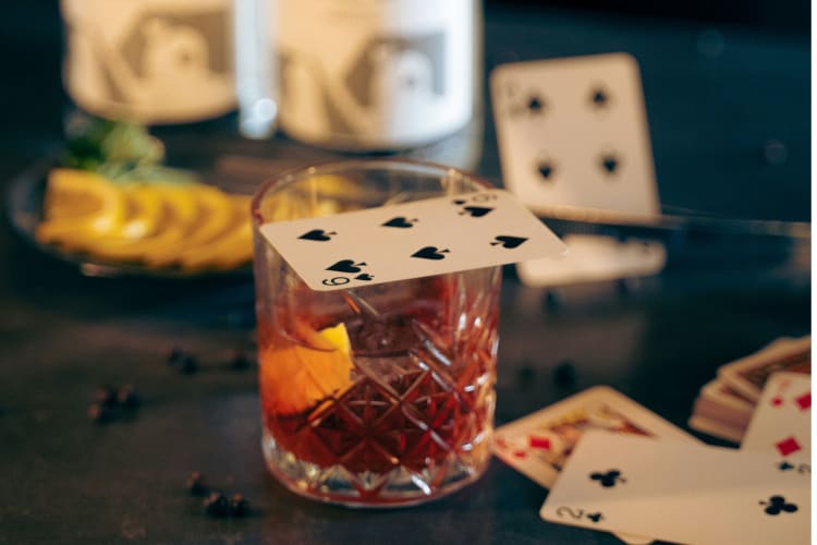 a cocktail sits with a playing card resting on top of it and others scattered around