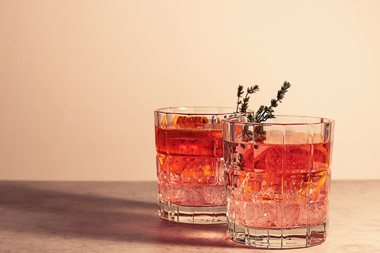 two red cocktails with lavender and ice garnish served in cut glasses