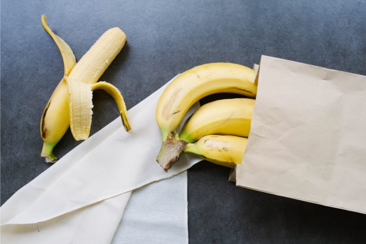 One peeled banana and bananas in a paper bag