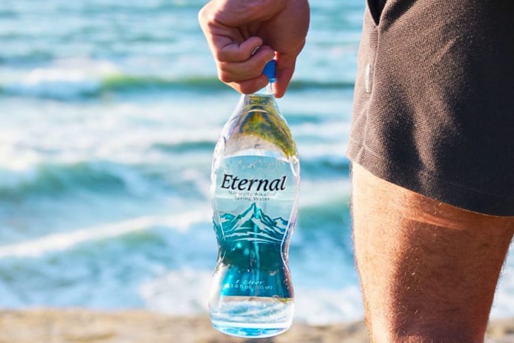 A man holding a water bottle at the beach.